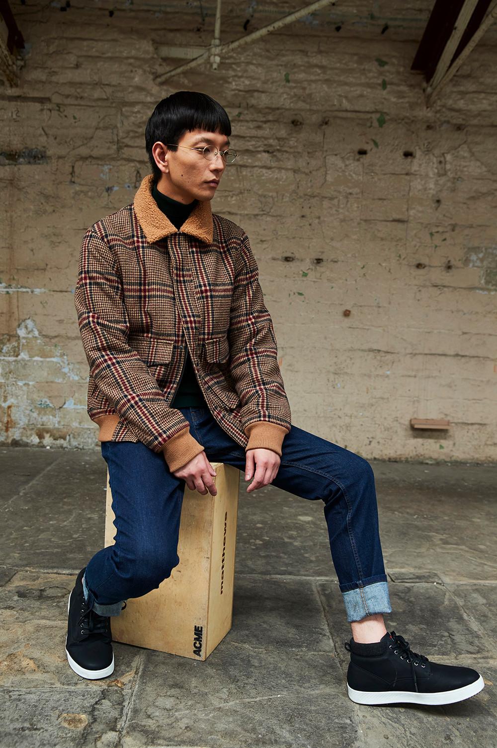 Model sits on box, wearing Checked Borg Aviator jacket, blue jeans and black shoes