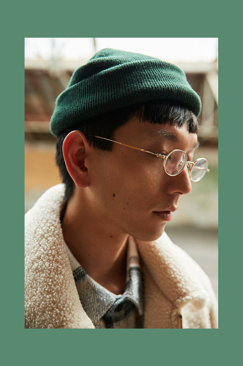 Close up portrait of model, looking down wearing glasses and a green beanie.