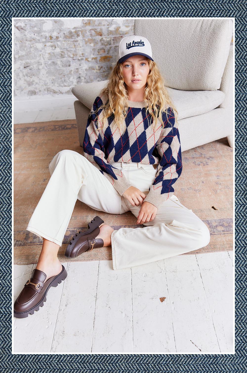 Model wears ecru jeans, patterned jumper and cap