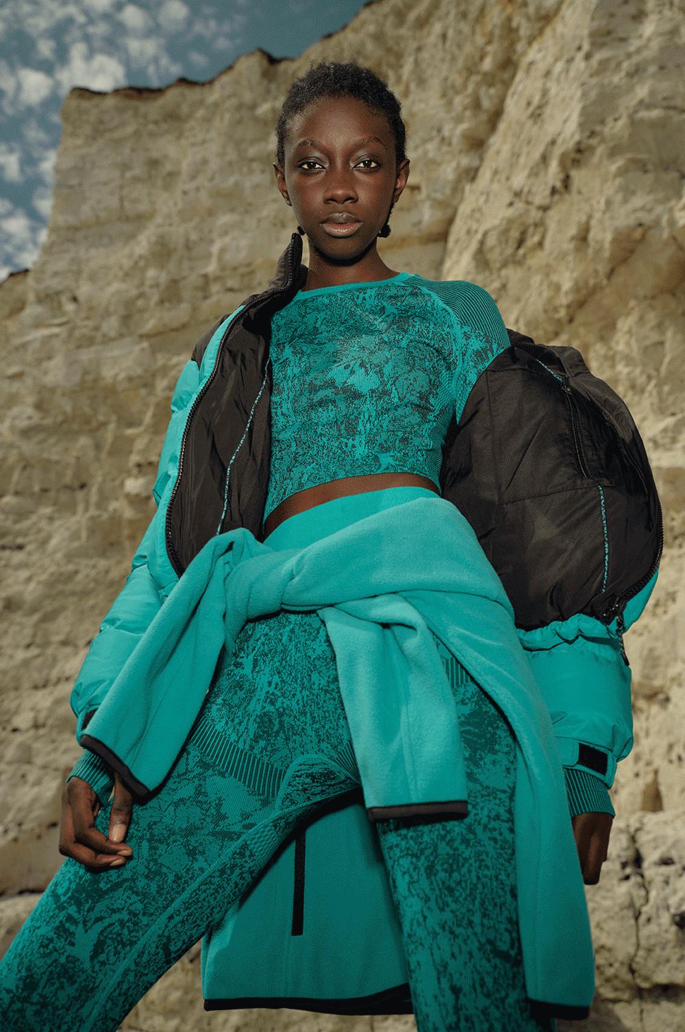 gif of model in teal puffer coat, wearing accessories such as the bum bag, walking boots and gloves