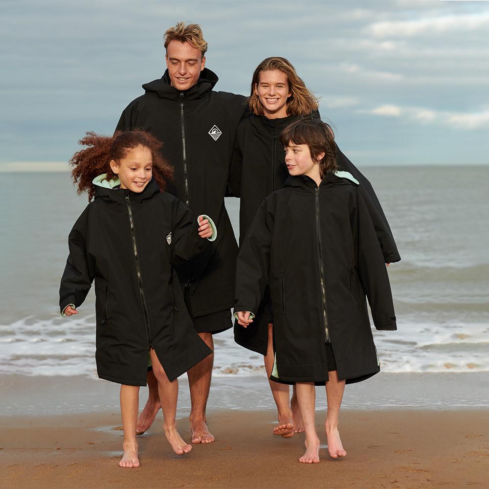 Famiglia che indossa giacche da surf nere in spiaggia