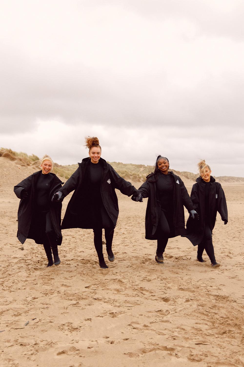 Influencer in schwarzen Trockenmänteln am Strand