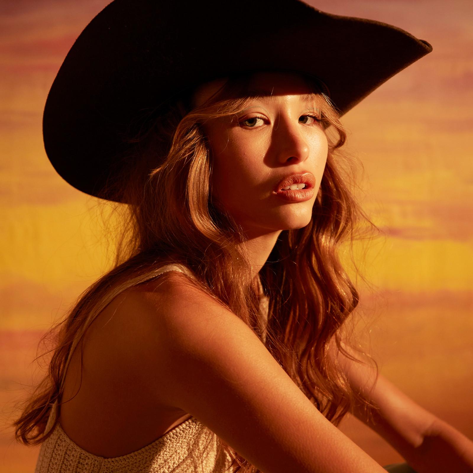 Model wears cowgirl hat and crochet top