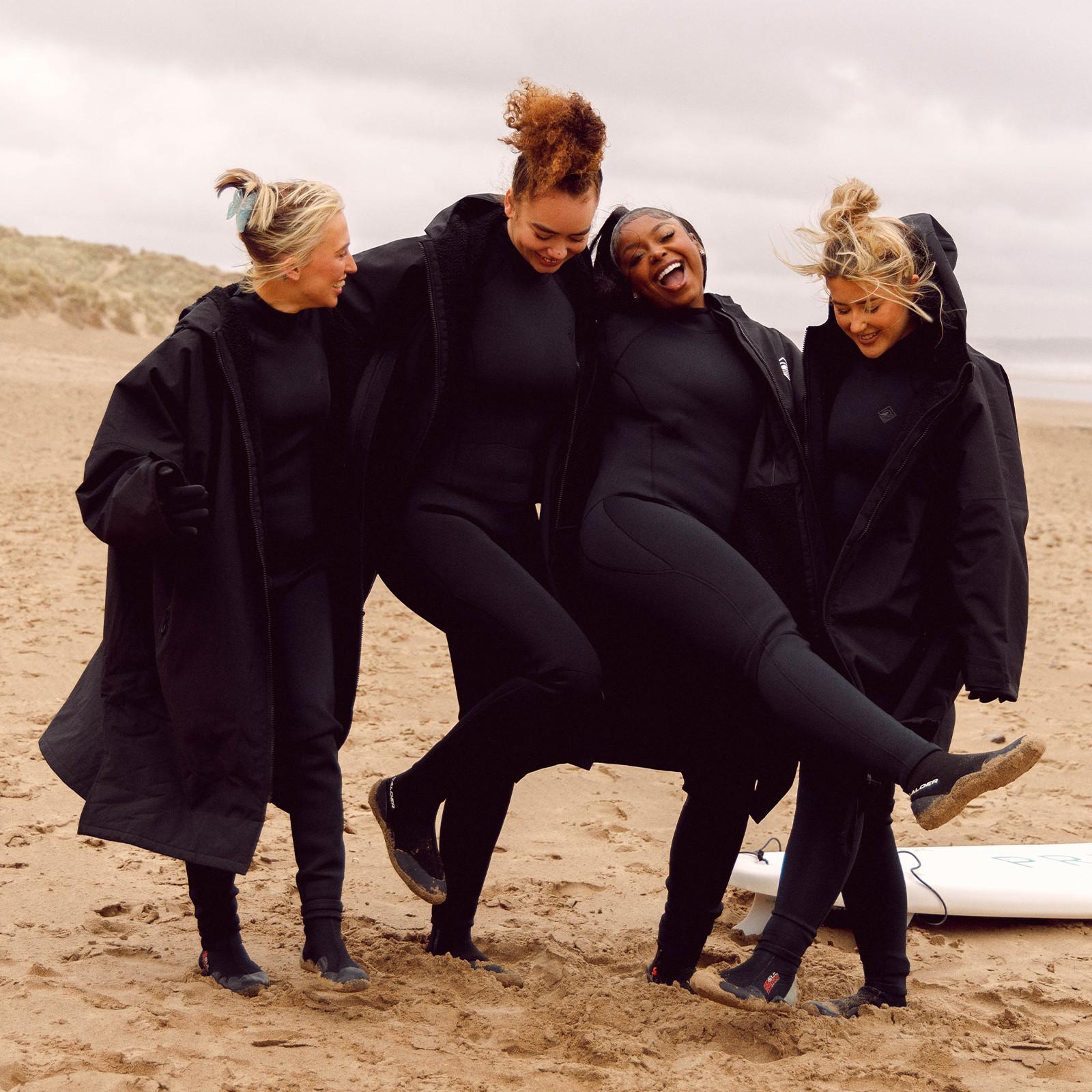 Influencer in schwarzen Trockenmänteln am Strand