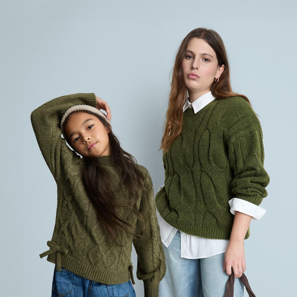 Two people wearing matching red pyjamas sitting on a pink sofa with wrapped gifts beside them.
