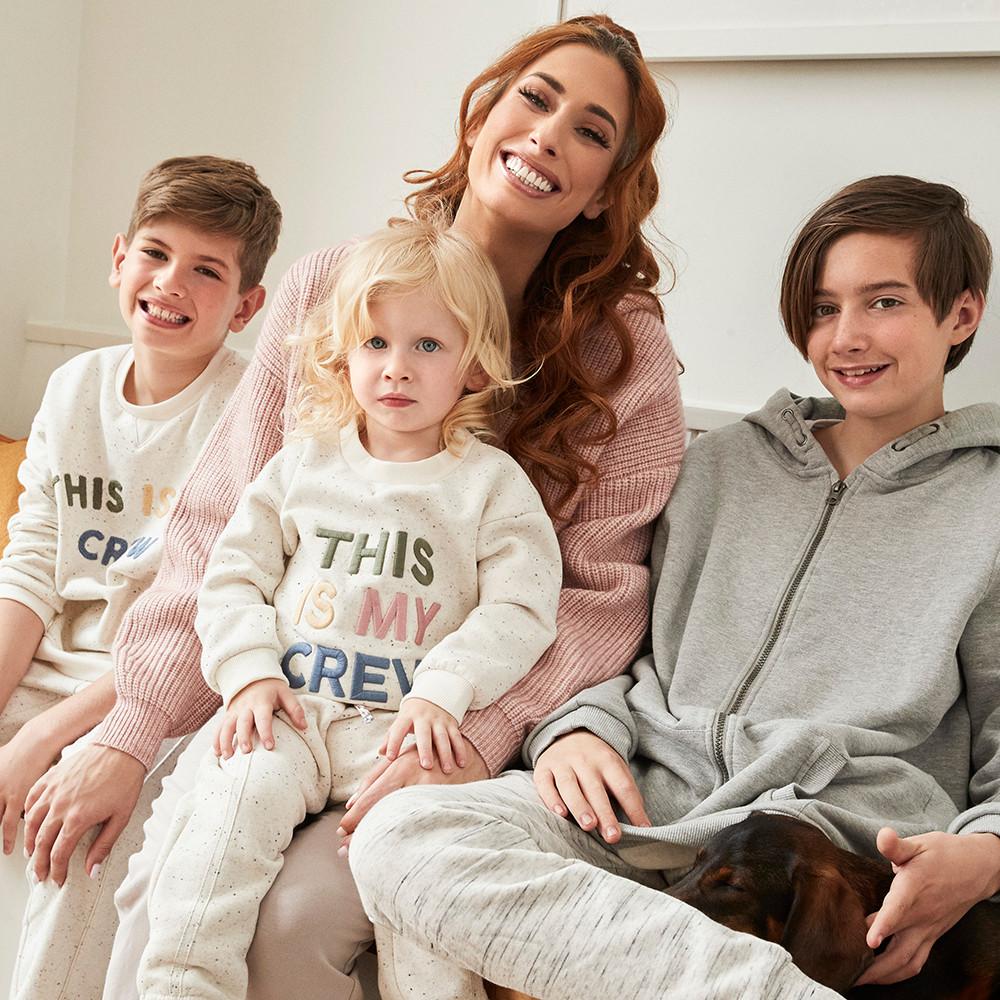 Stacey sits with two of her boys, smiling whilst they wear the ecru "this is my crew" sweatshirt
