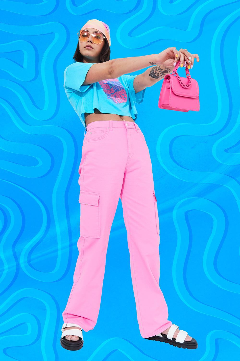 Modelo veste calças cargo rosa-choque, combinadas com top curto azul e lenço no cabelo