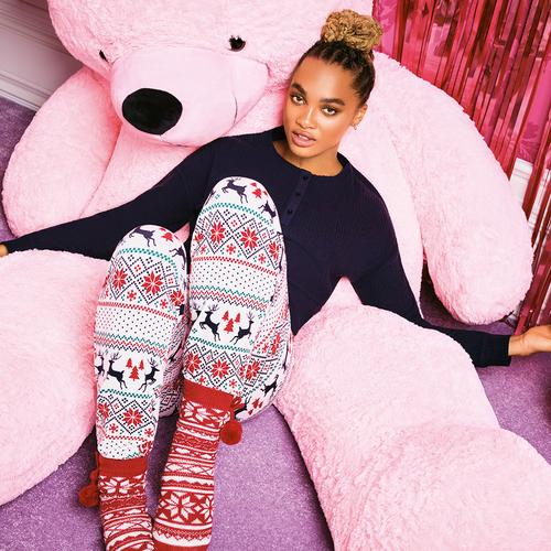 Model trägt weihnachtliche Pyjamas, während es vor einem riesigen pinken Bären sitzt