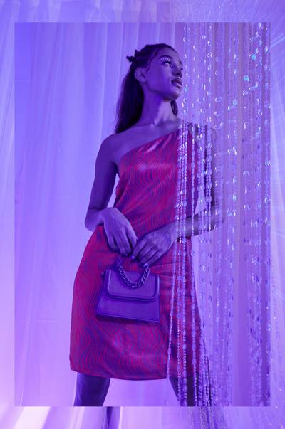 Model draagt een paarse tas en roze glanzende mini-jurk met blote schouder