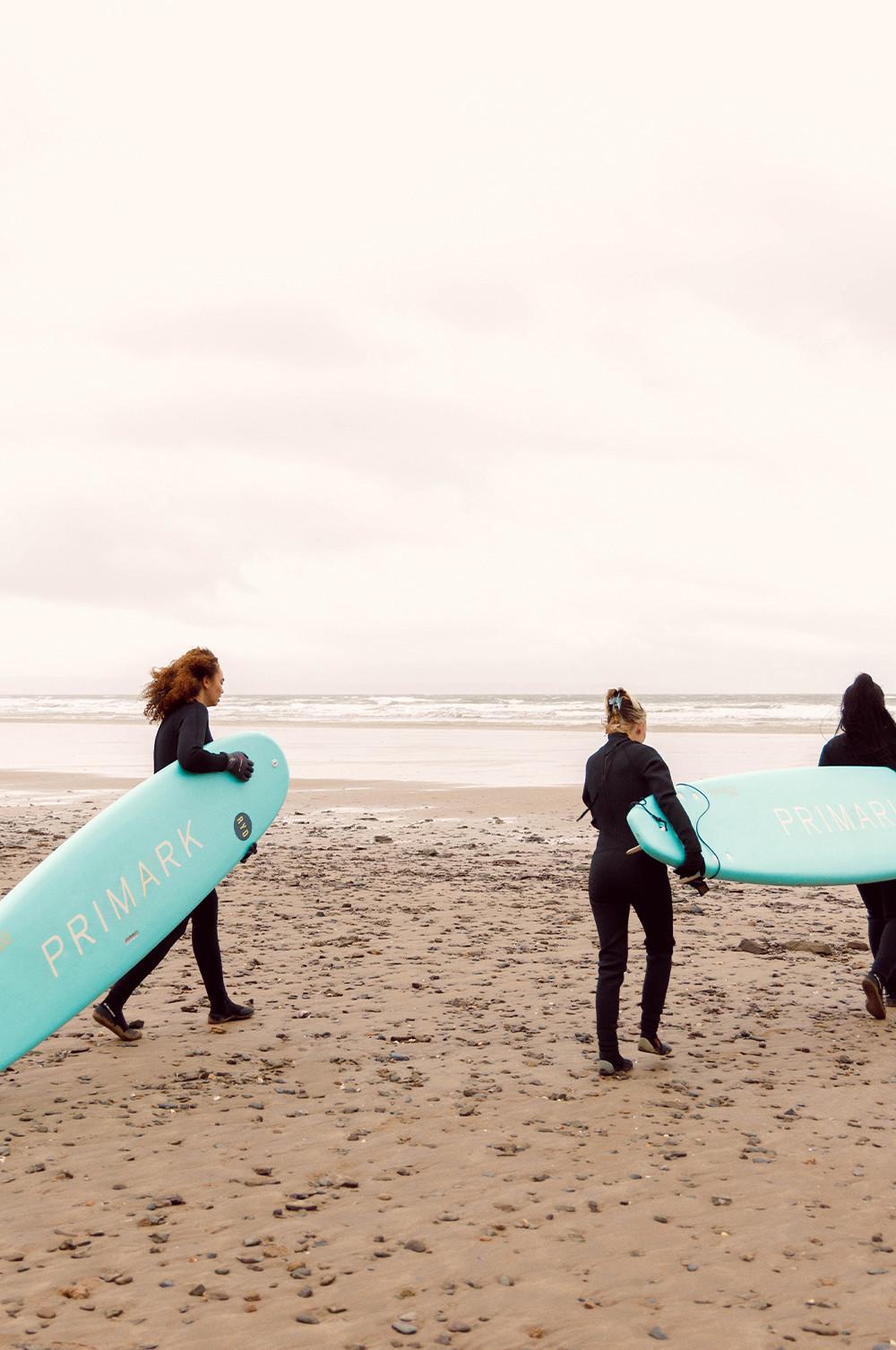 Influencer gehen mit Primark Surfbrettern am Strand spazieren