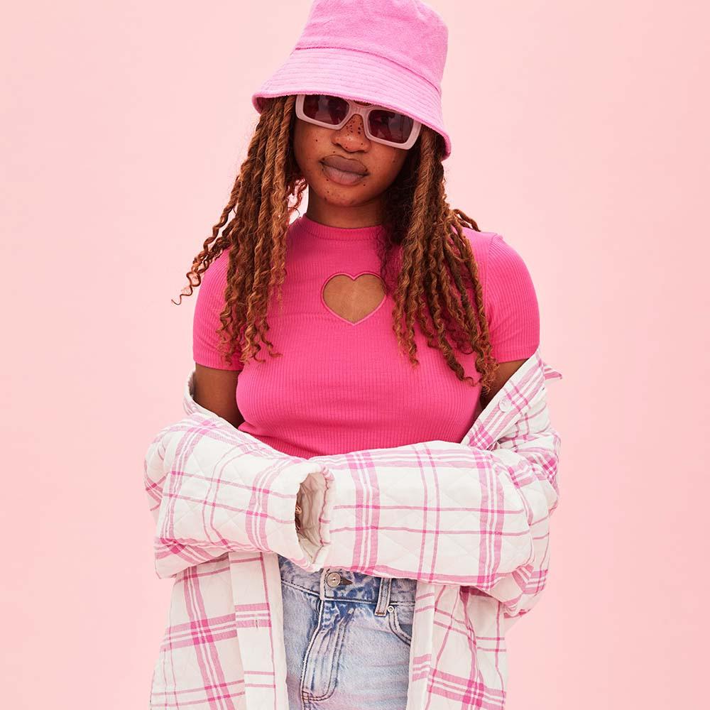 Model wears hot pink top with heart shaped cut out, paired with a pink checked shacket and hat