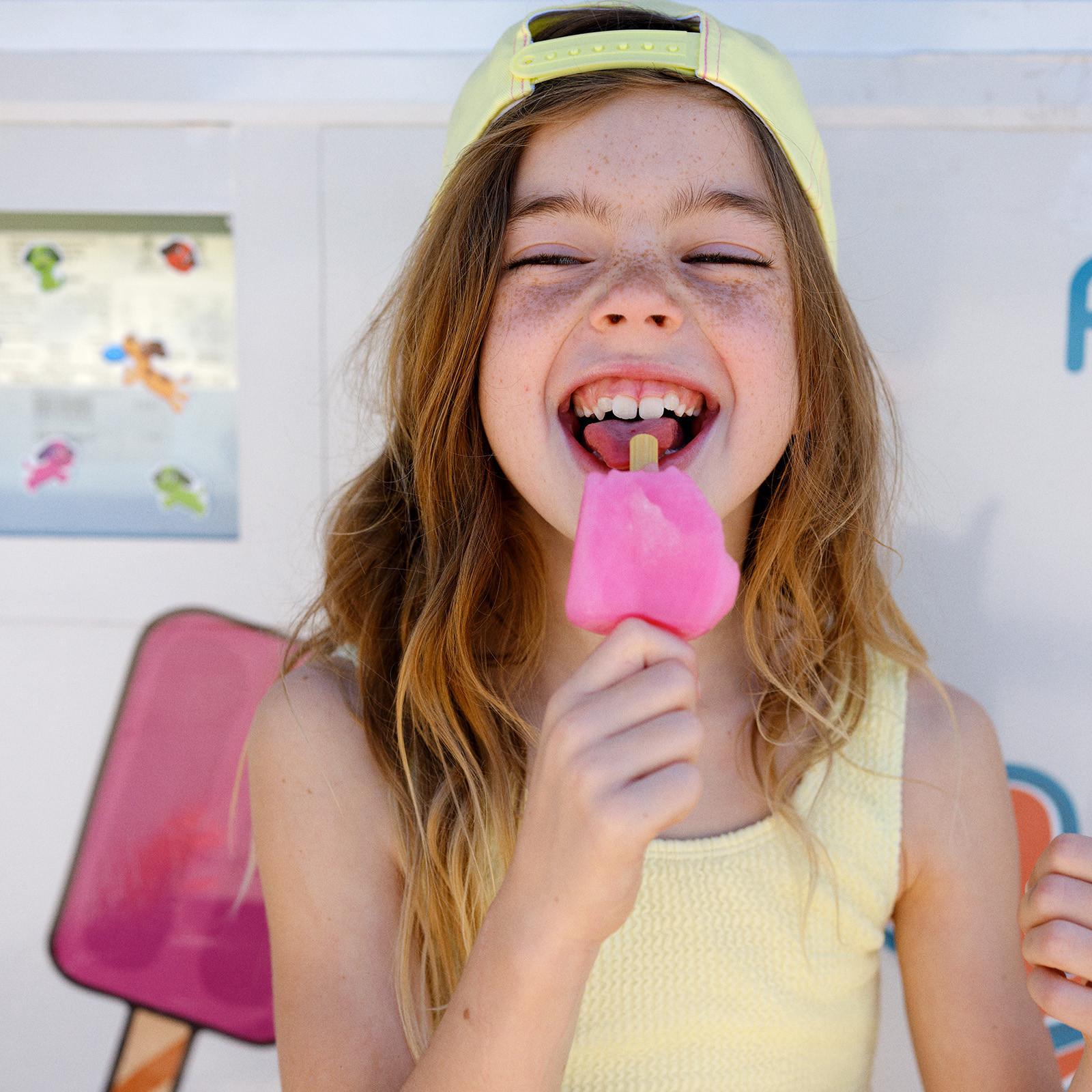 Criança a sorrir com gelado na mão e boné e top amarelo