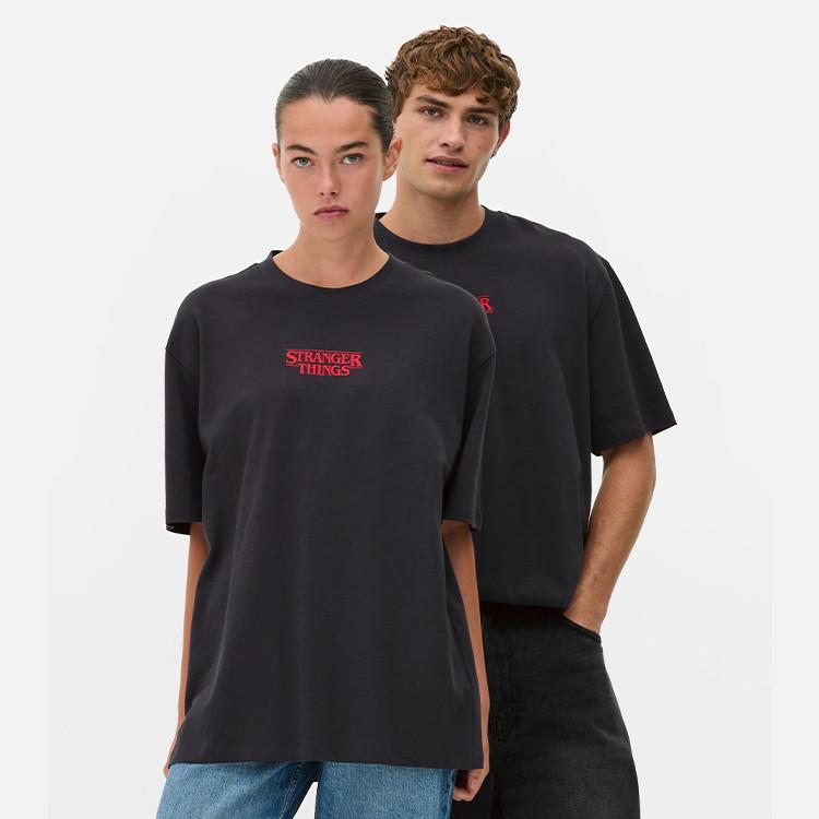 Two people wearing black Stranger Things t-shirts with red logo, one in blue jeans.
