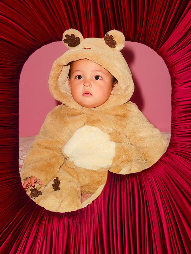 Soft teddy bear costume with hood and paw details against a red pleated backdrop.