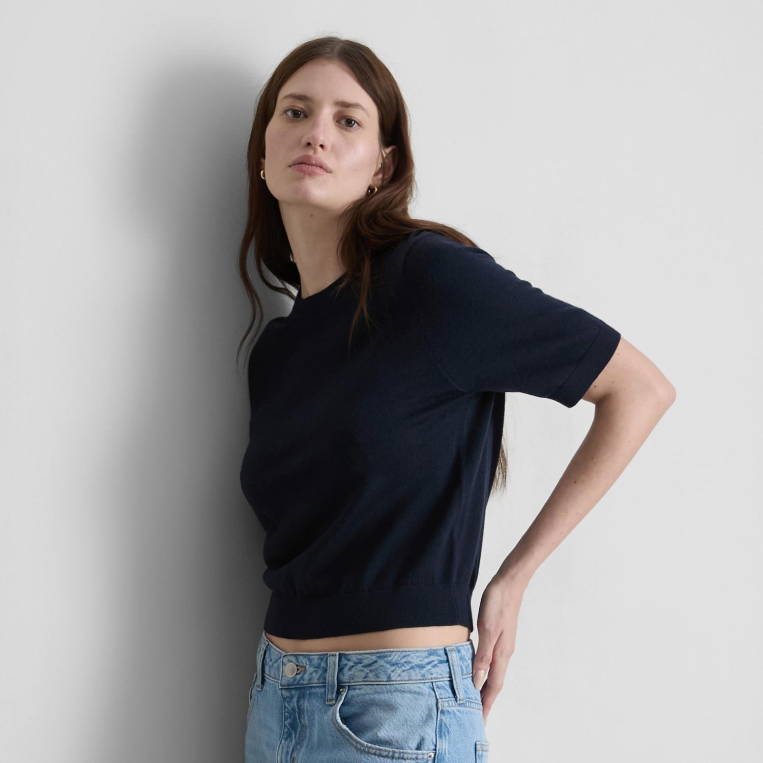 Person wearing a navy blue short-sleeve top with light blue denim jeans against a white background.