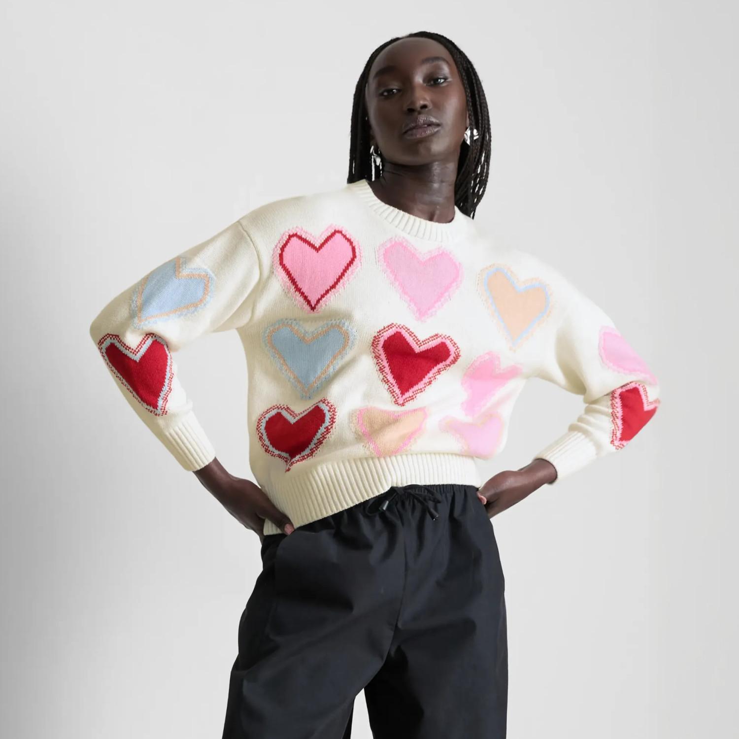 Cream jumper decorated with multicoloured heart patterns, paired with black trousers.