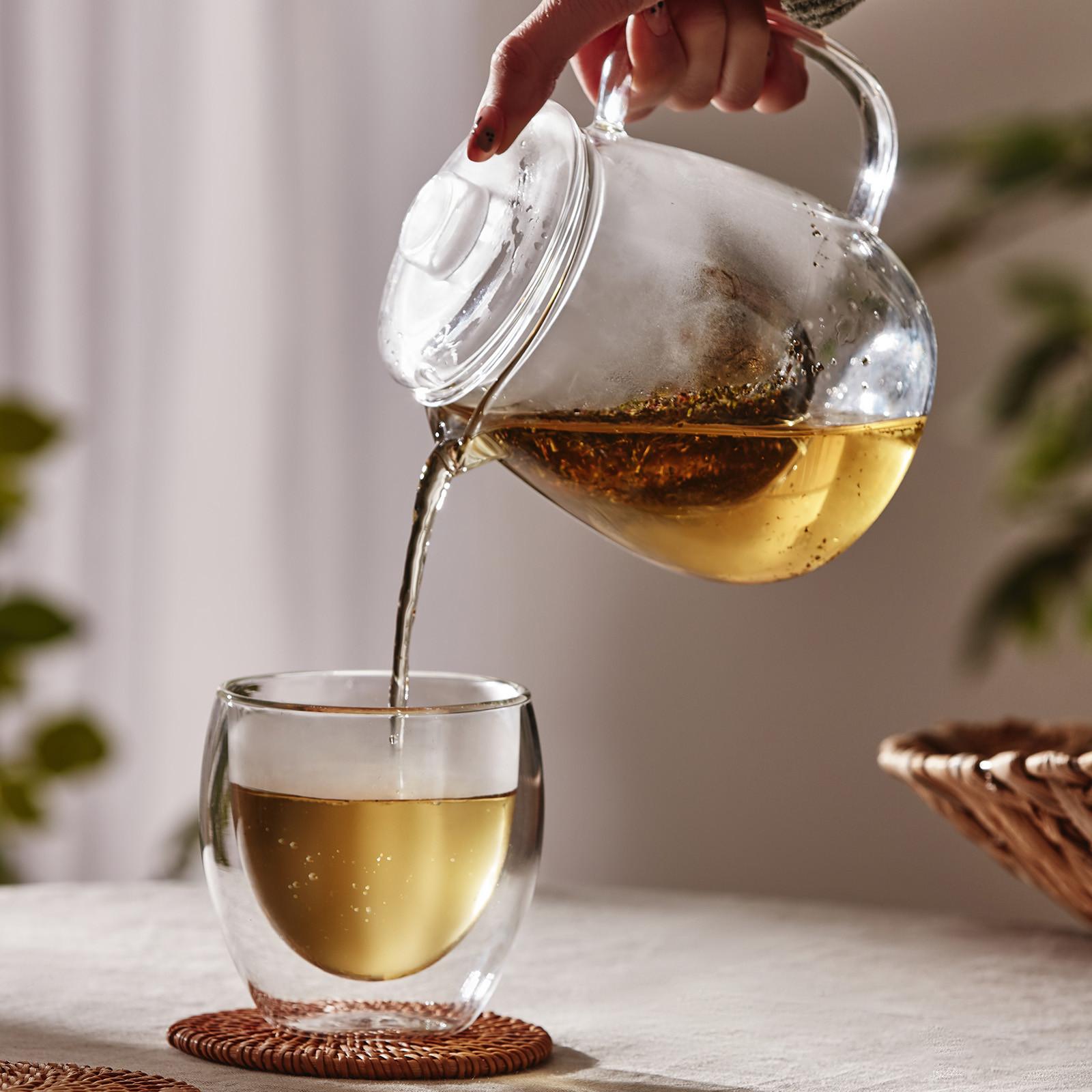 Glass teapot pouring tea into glass mug