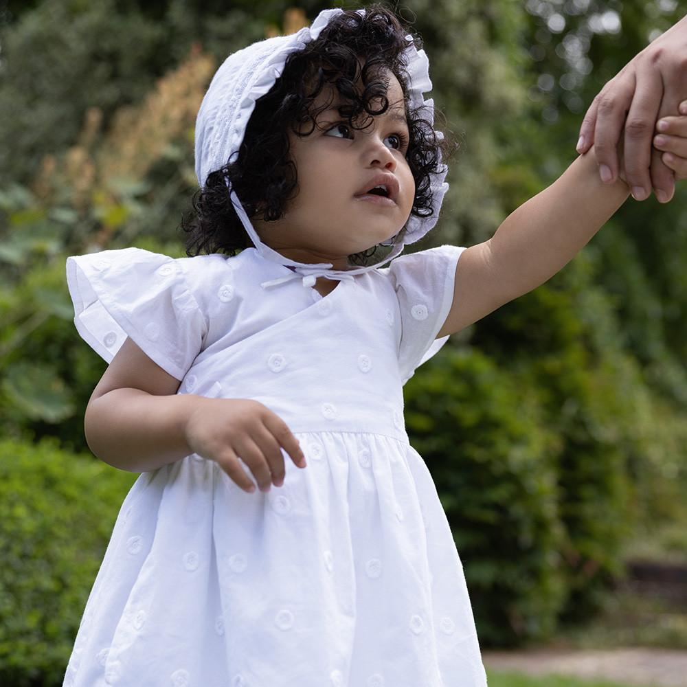 Kind in weißem Kleid und Haube mit Stickerei