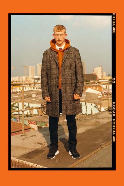 Modelo com um casaco em xadrez largo e camisola com capuz cor de laranja