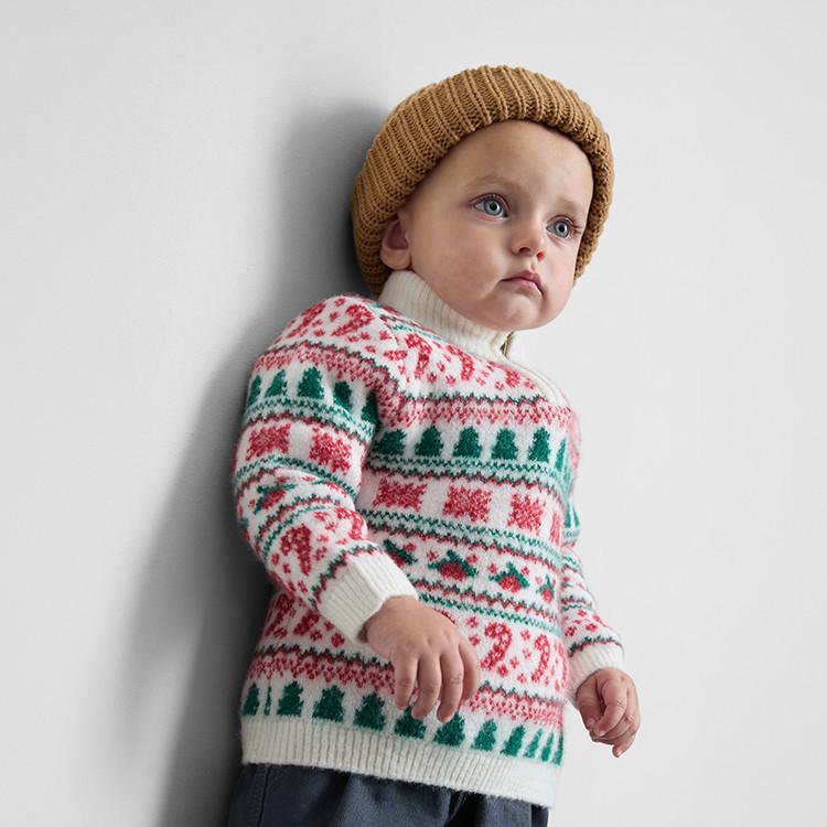 Child wearing festive Christmas jumper with green trees and red patterns, paired with a brown knitted beanie.