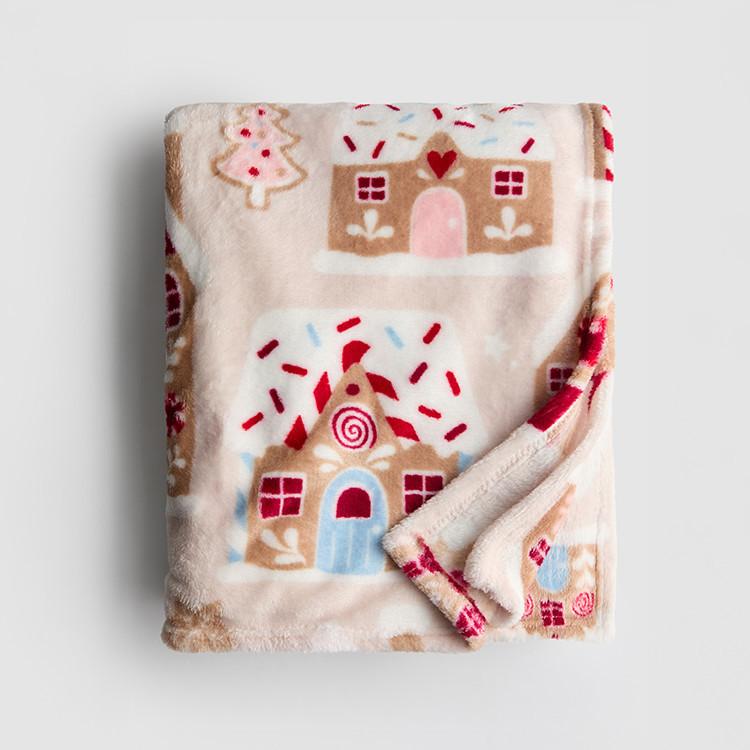 Soft cream fleece blanket with festive gingerbread house and Christmas tree pattern, corner folded.