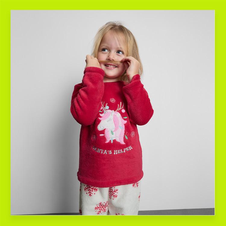 Child wearing red Christmas jumper with unicorn design and white pyjama bottoms with snowflake pattern.