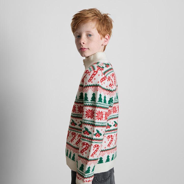 Child wearing cream turtleneck Christmas jumper with festive pattern of trees, snowflakes and candy canes.