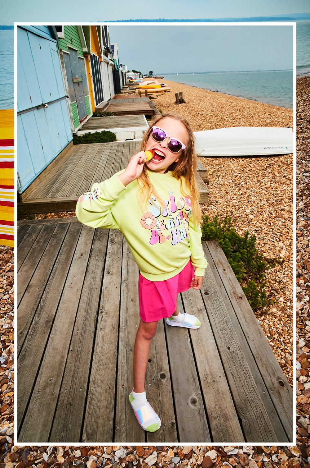 Child wearing a pink tennis skirt and a yellow graphic sweatshirt